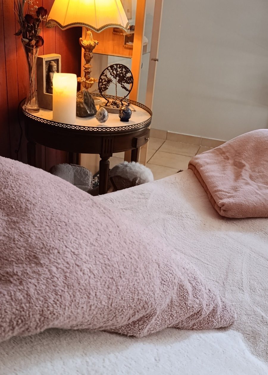 Table de soins avec des couleurs chaleureuses, un oreiller et une couverture. Eclairage doux avec une lampe et une bougie